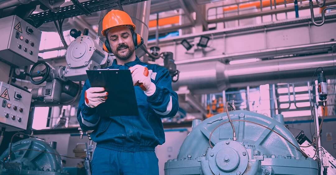 Man with hard hat and headphones writing with clipboard